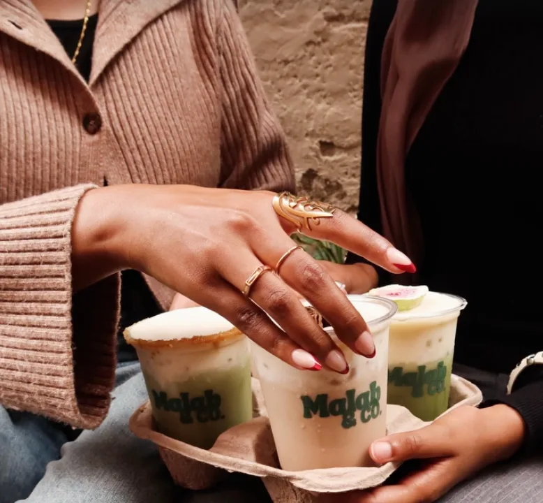 Hands with gold rings lifting a Malab cup from a carrier of fall drinks
